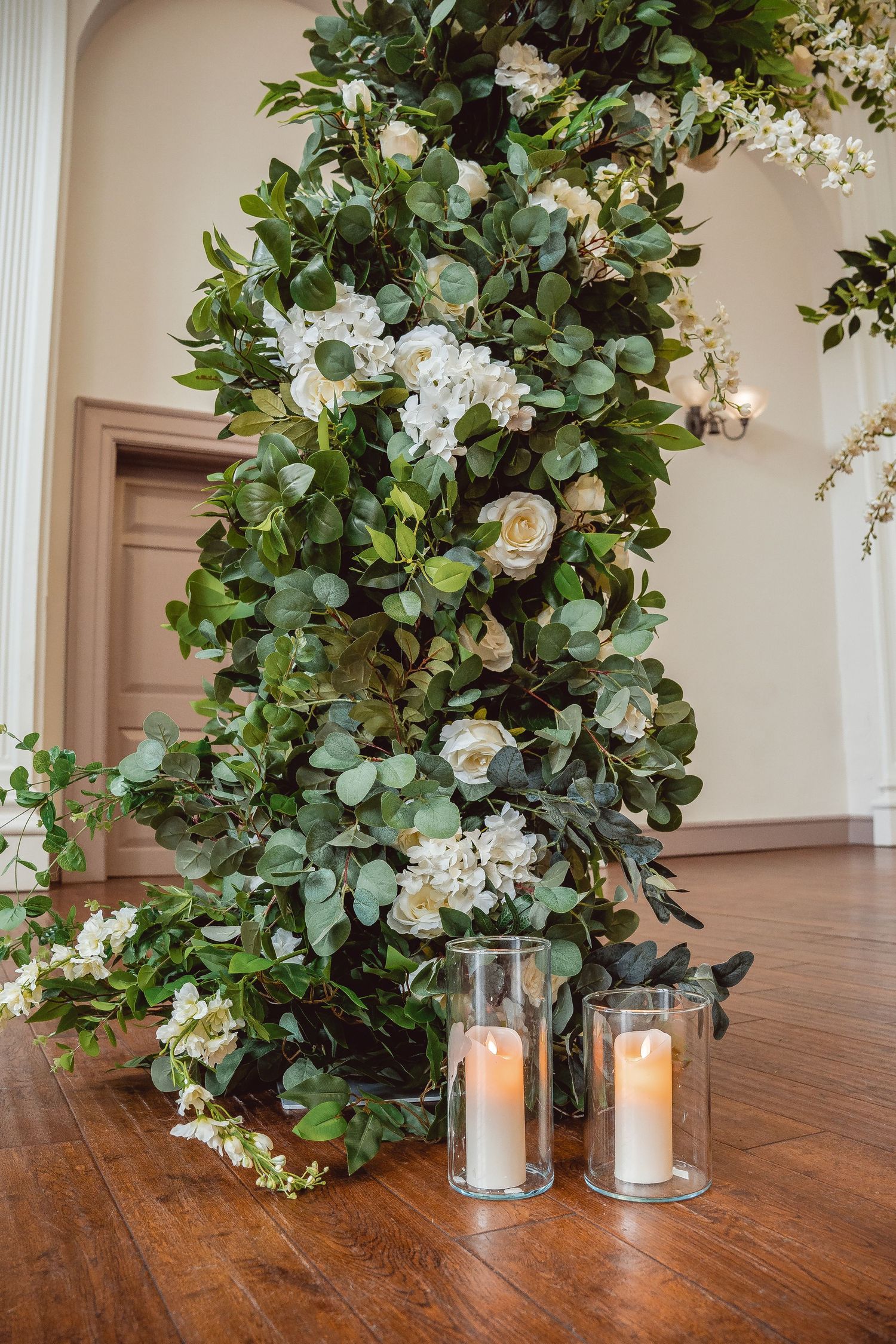Close up of ceremony decor made of foliage and white flowers and pillar candles at the base