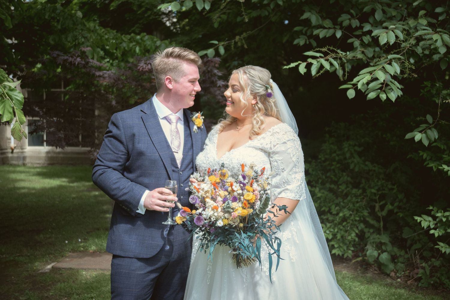 Newlyweds sharing champagne outdoors while holding vibrant orange and blue wedding bouquet.