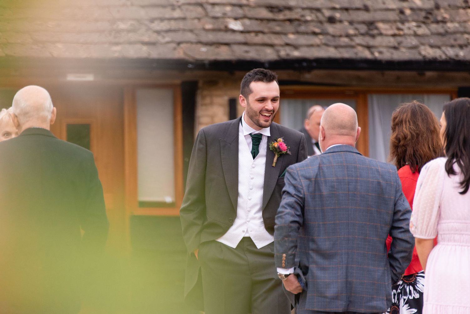 Wedding reception guests mingling outside a traditional stone building.