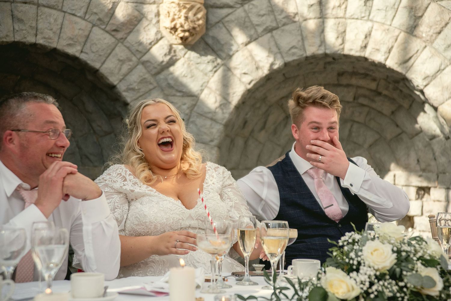 Wedding party enjoying speeches and laughter at stone venue reception.