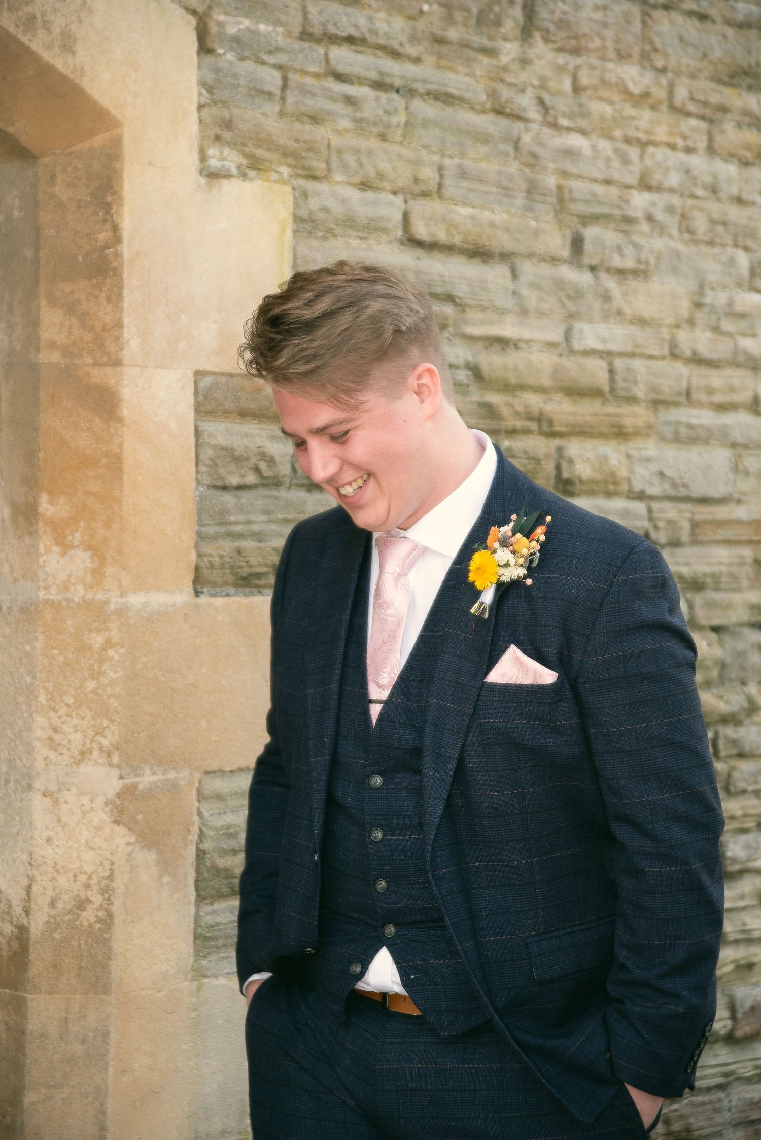 Close-up shots of a groomsman in navy suit with pink tie against a stone wall.