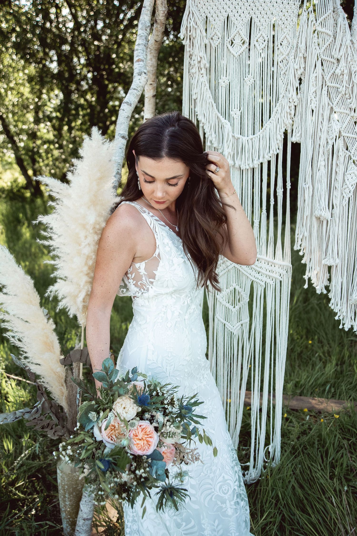 Elegant bridal portrait showcasing a lace wedding gown and floral bouquet against macrame decor.