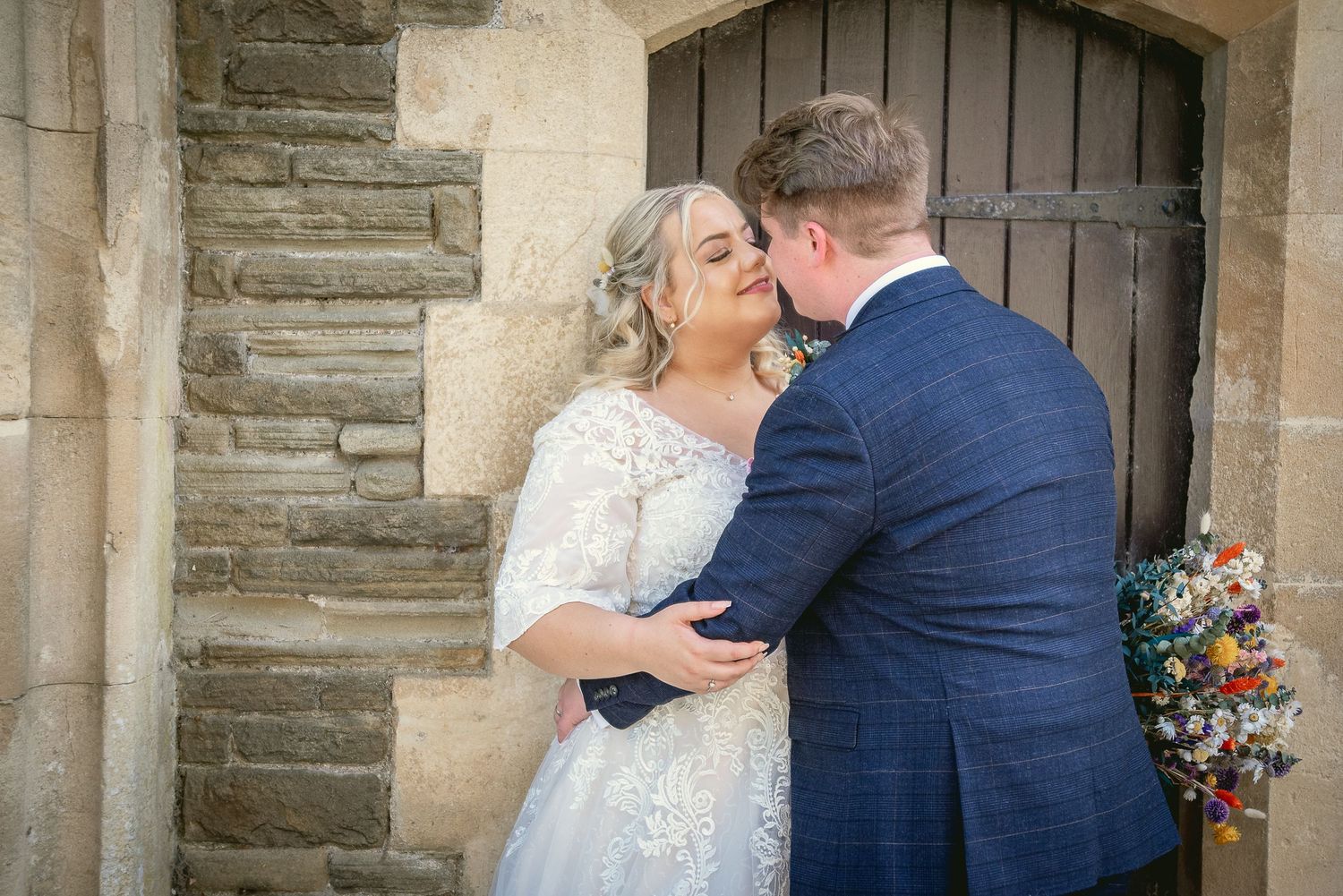 A romantic moment shared between newlyweds against a rustic stone wall backdrop.