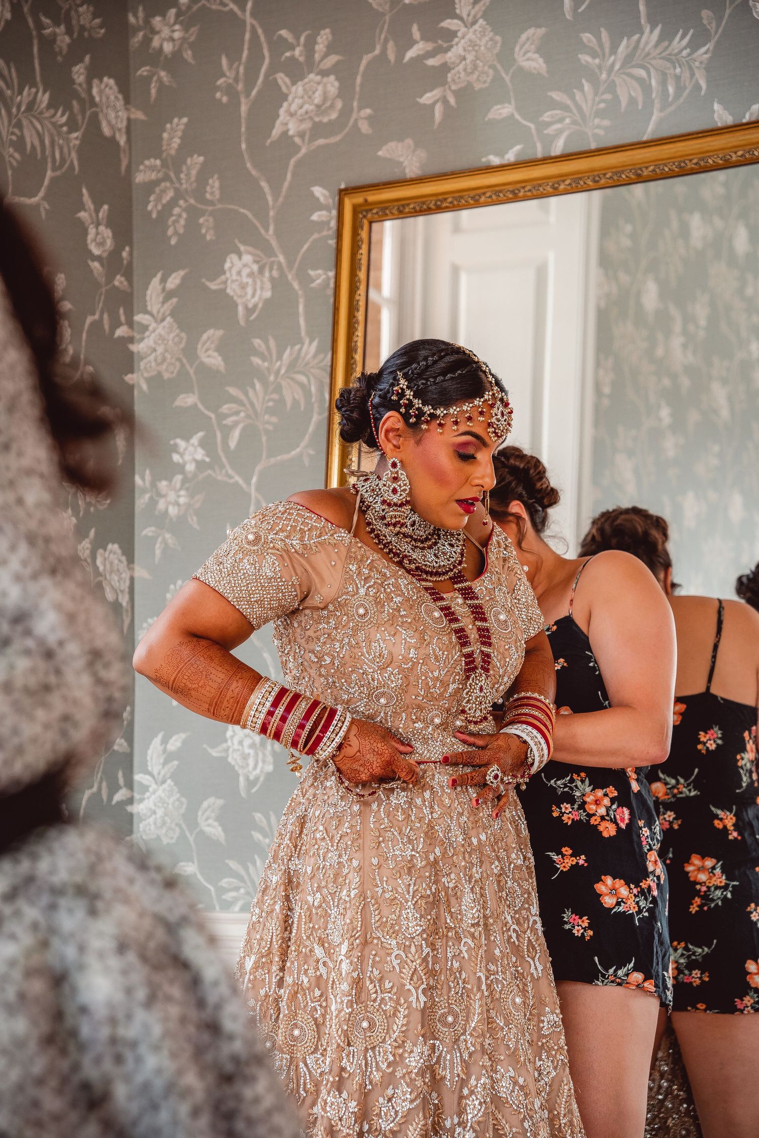 Indian bride with red and gold saree outfit being helped by a bridesmaid