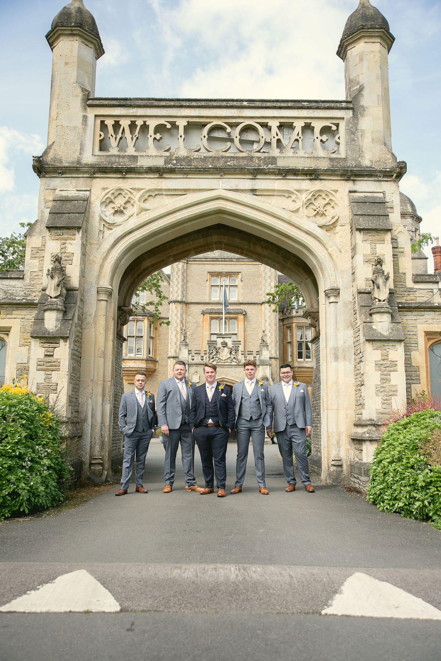 Group photos of groomsmen standing beneath a stone welcome arch at a wedding venue.