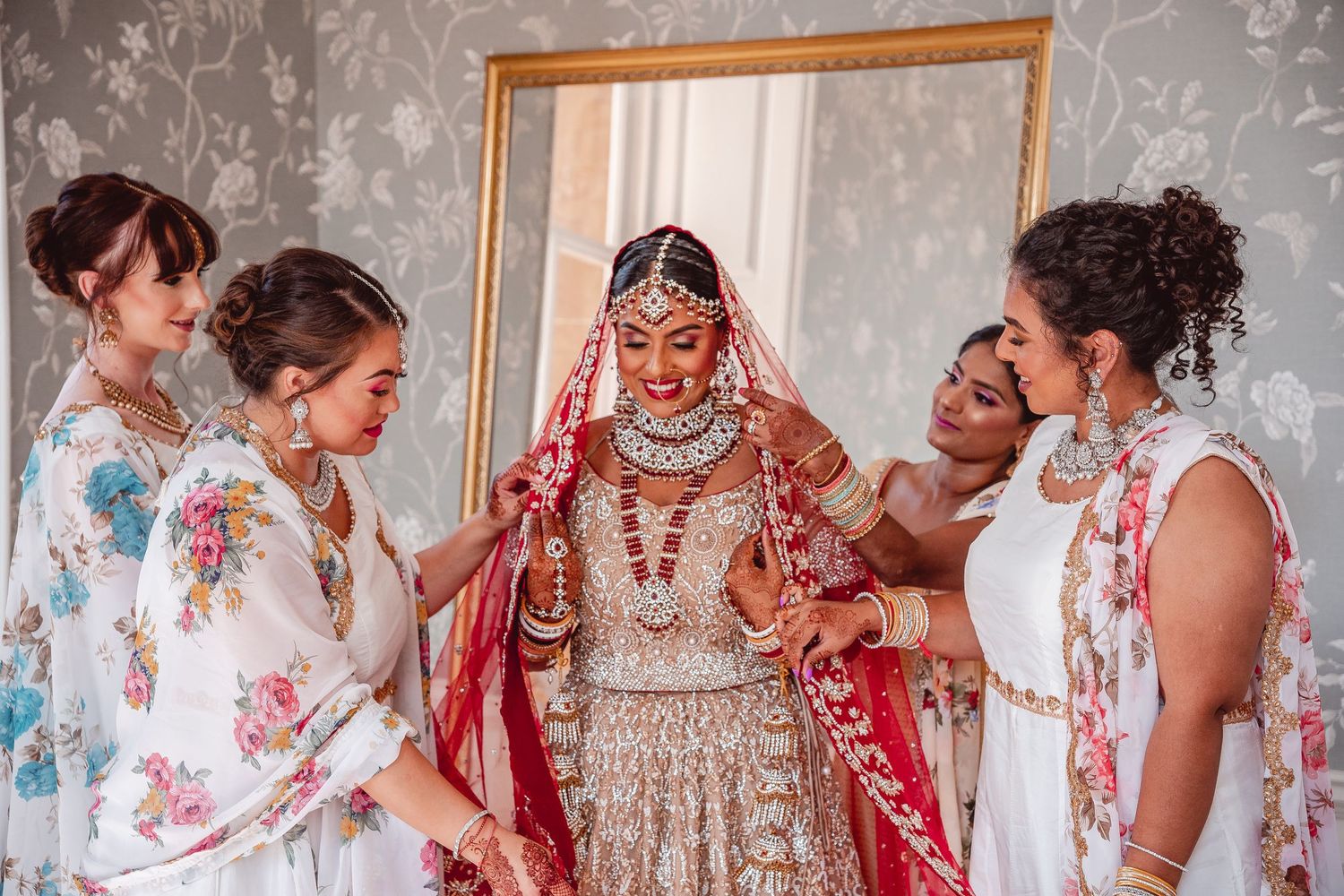 Indian Bride in Red and Gold being helped getting ready by her bridesmaids