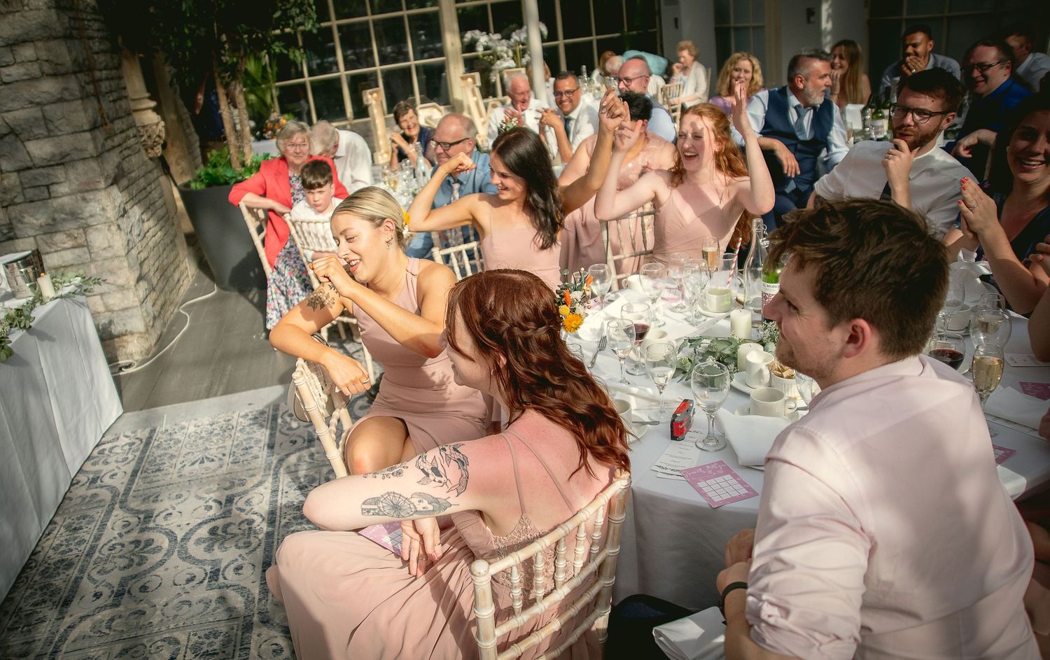Wedding reception guests celebrating with raised glasses in elegant stone venue.
