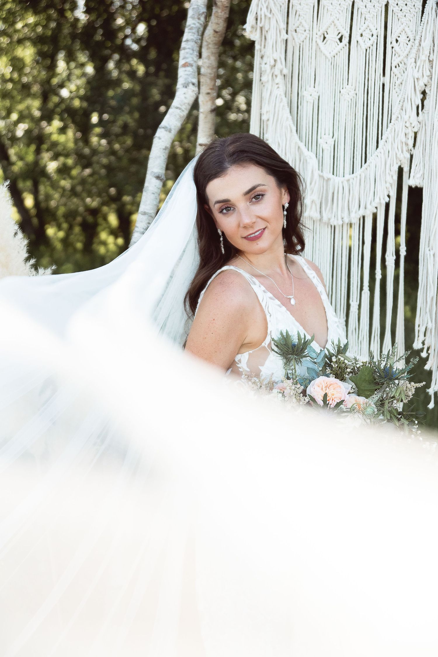 Romantic bridal portrait with soft lighting and white macrame backdrop in an outdoor setting.