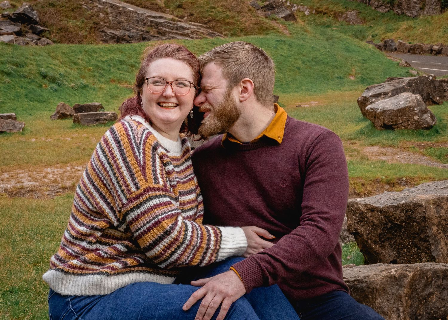 close up of couple sat down and embracing, woman looking away smiling as man whispers something in her ear