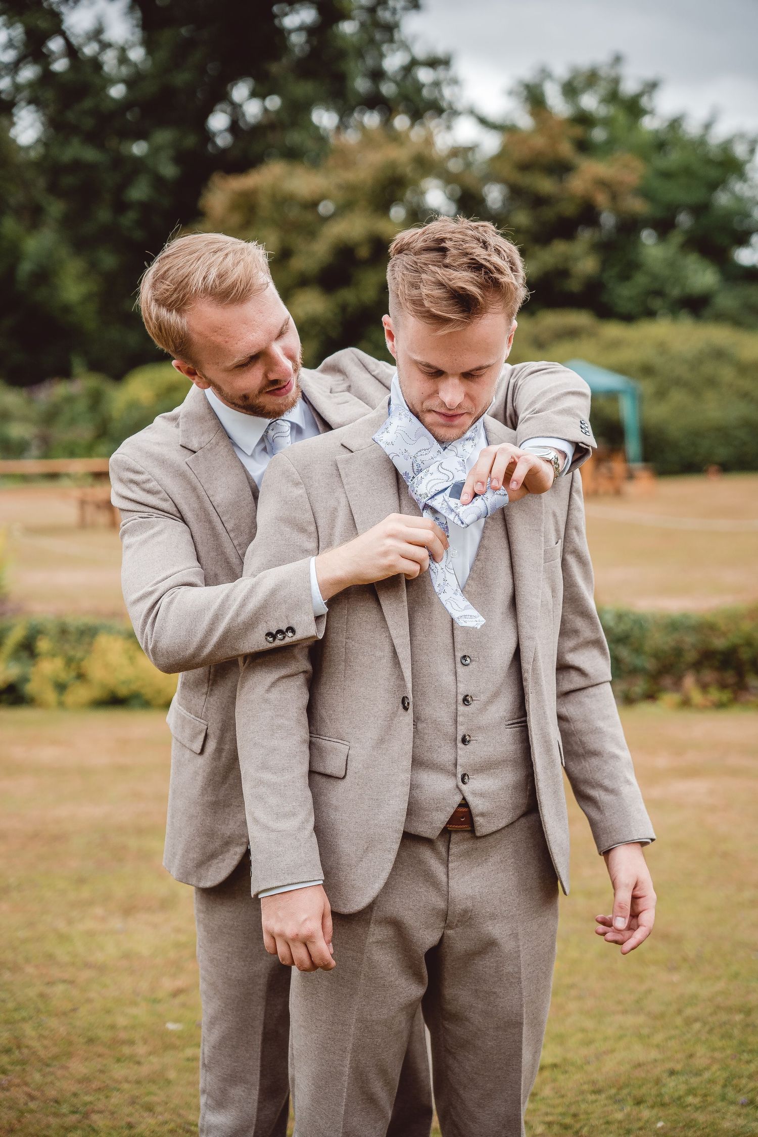 Groomsmen helping each other tie their ties - oatmeal coloured suits and light blue ties