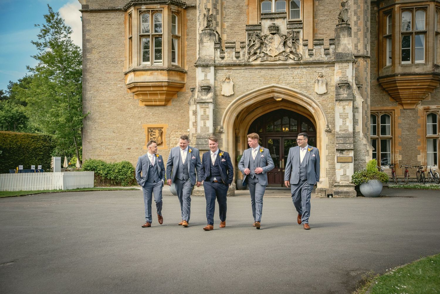 Wedding party in coordinated gray suits poses in front of a historic stone building.