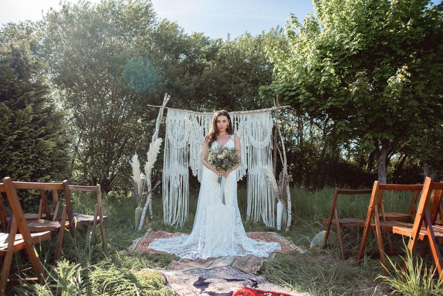 Wedding ceremony setup with macrame backdrop and wooden chairs in a garden setting.