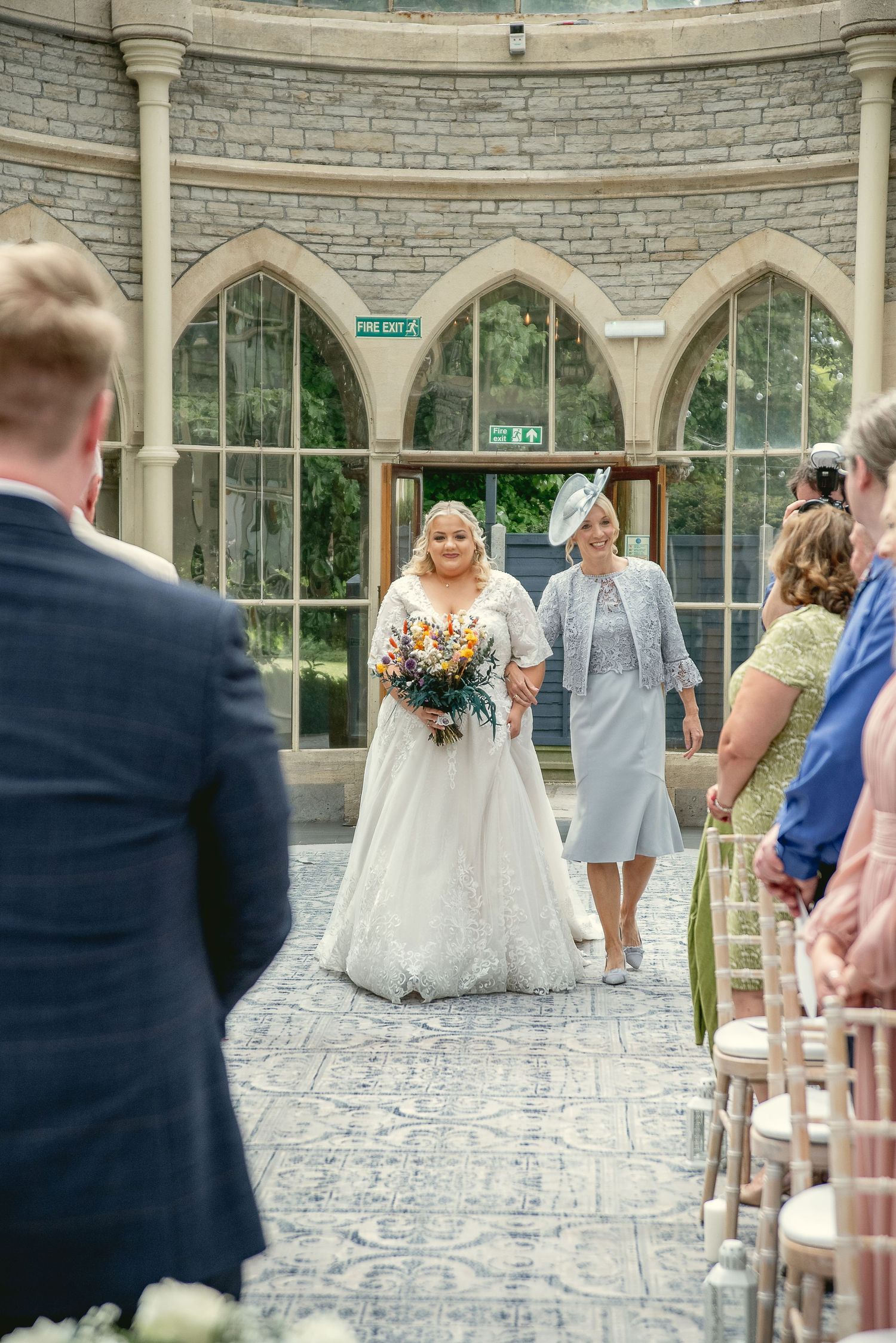 Wedding ceremony setup in an elegant stone conservatory with arched windows.