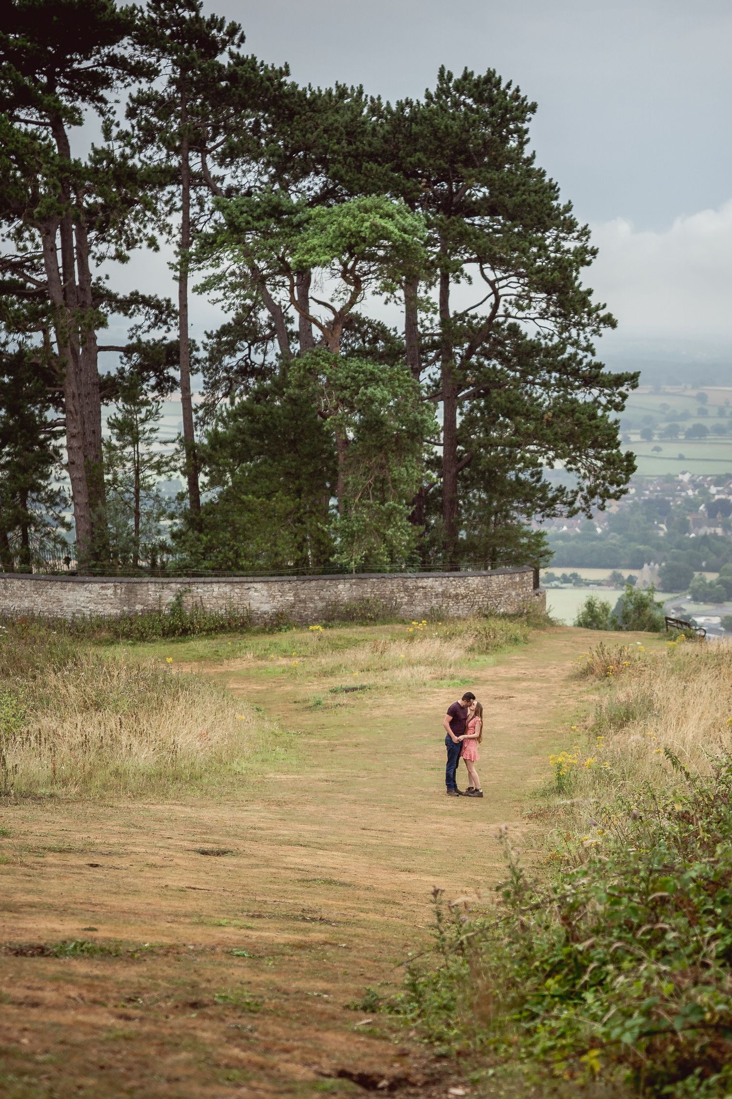 wide shot of couple kissing in the distance on the tree-covered hill with views of the valley below