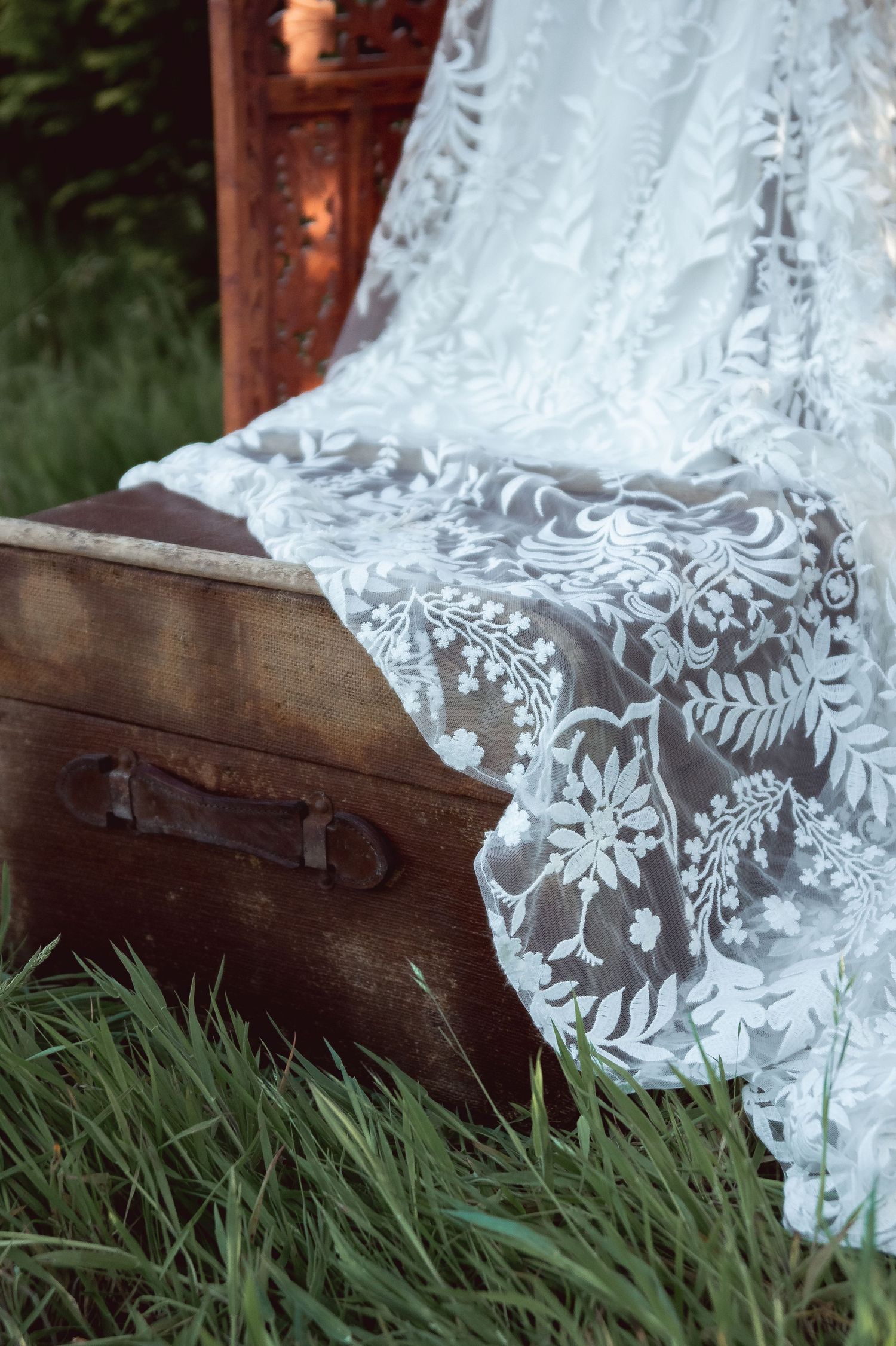 Delicate white lace fabric with floral patterns draped over grass in natural lighting.