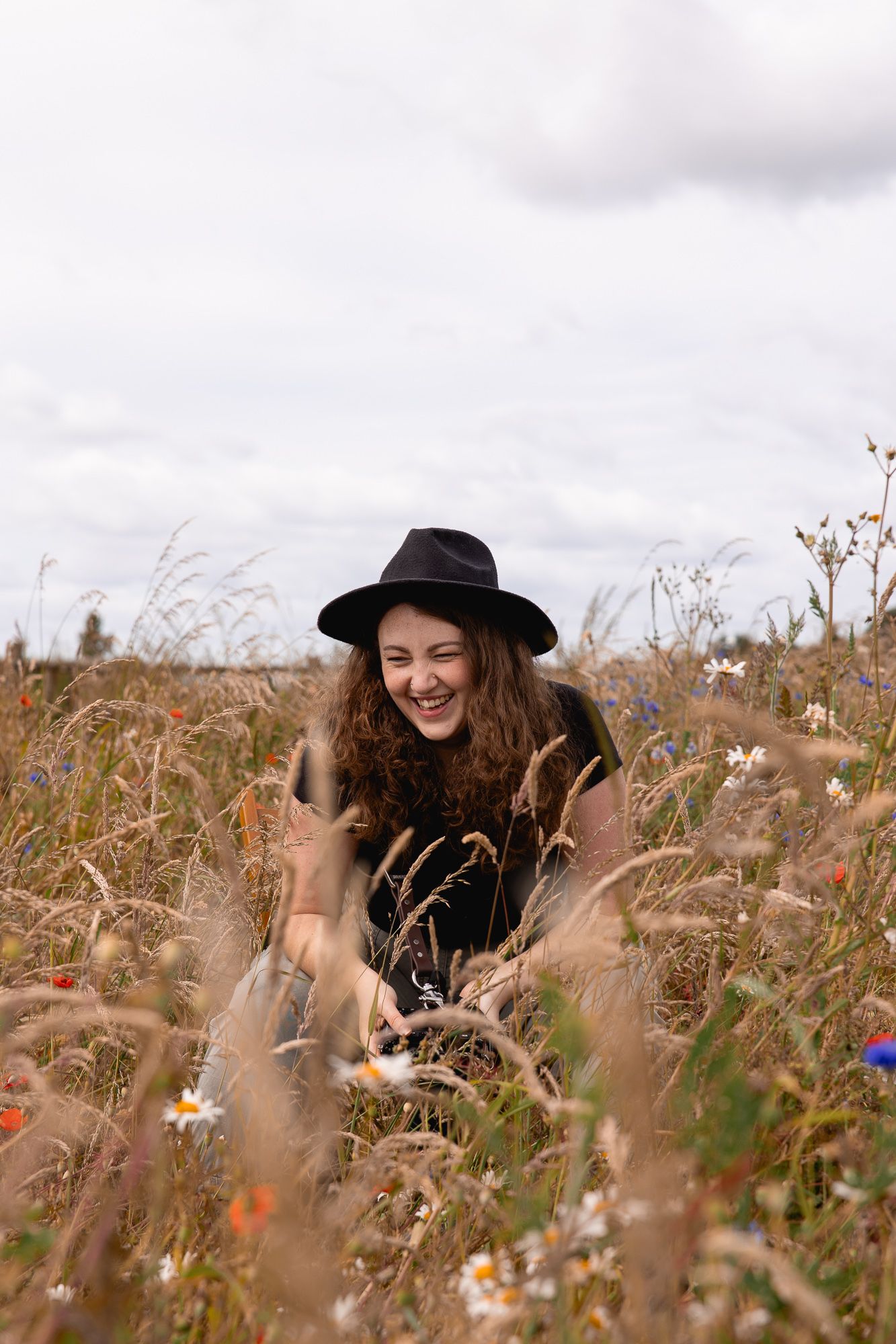 Person in black hat photographing in a wildflower meadow on an overcast day.