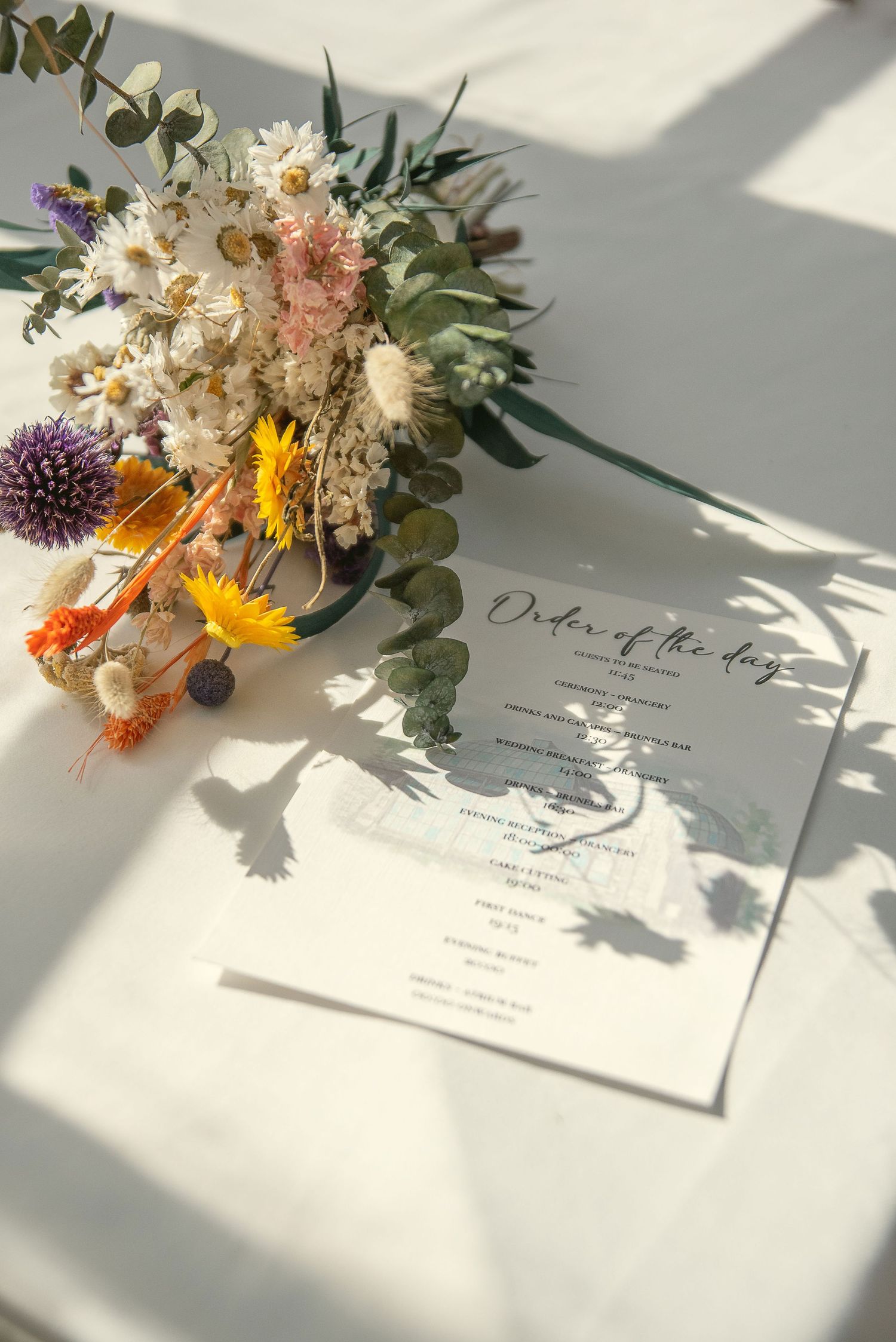 Colorful wildflower arrangements next to wedding menus on a white tablecloth.