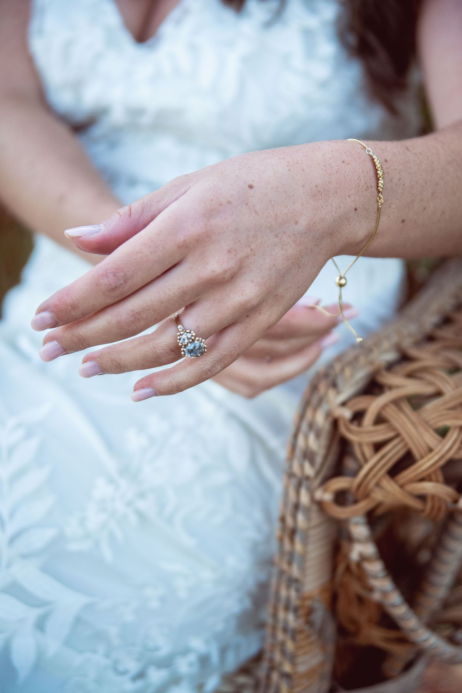 Close-up of delicate jewelry and rings on hands against white lace dress fabric.