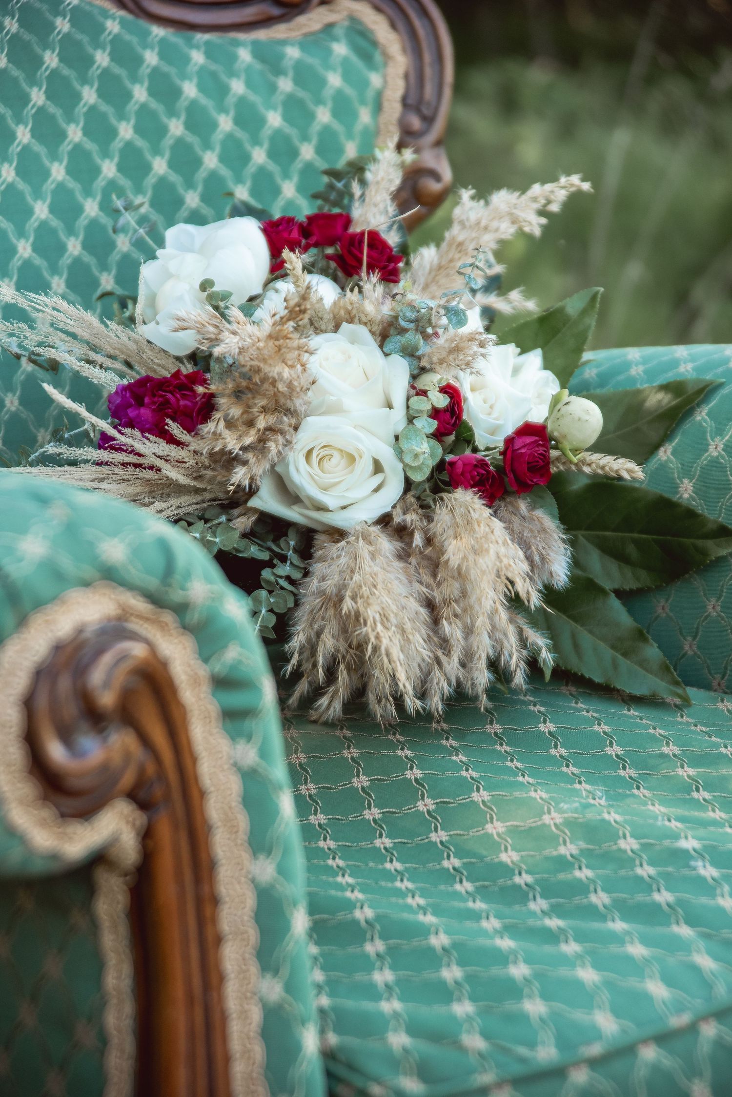 Wedding floral arrangement with white roses and burgundy flowers on a teal patterned surface.