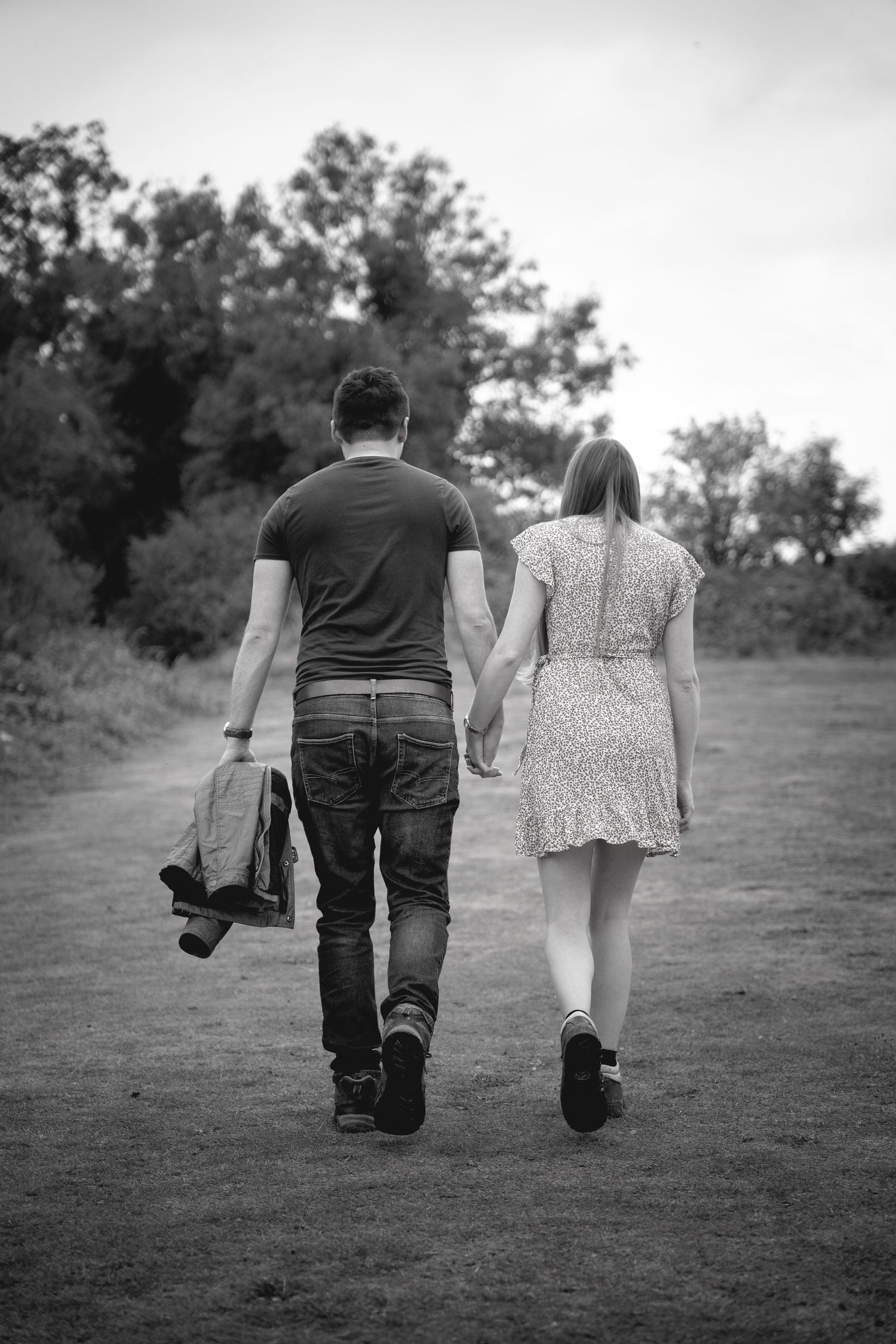 black and white image of couple walking away holding hands up the hill