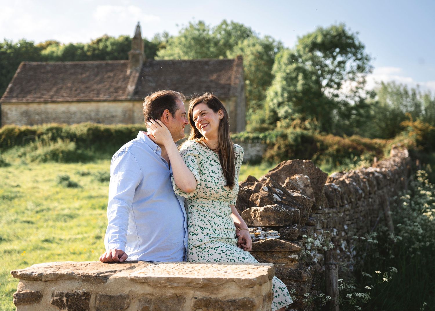 couple sitting on a rural wall in a field at sunset, a church is in the distance