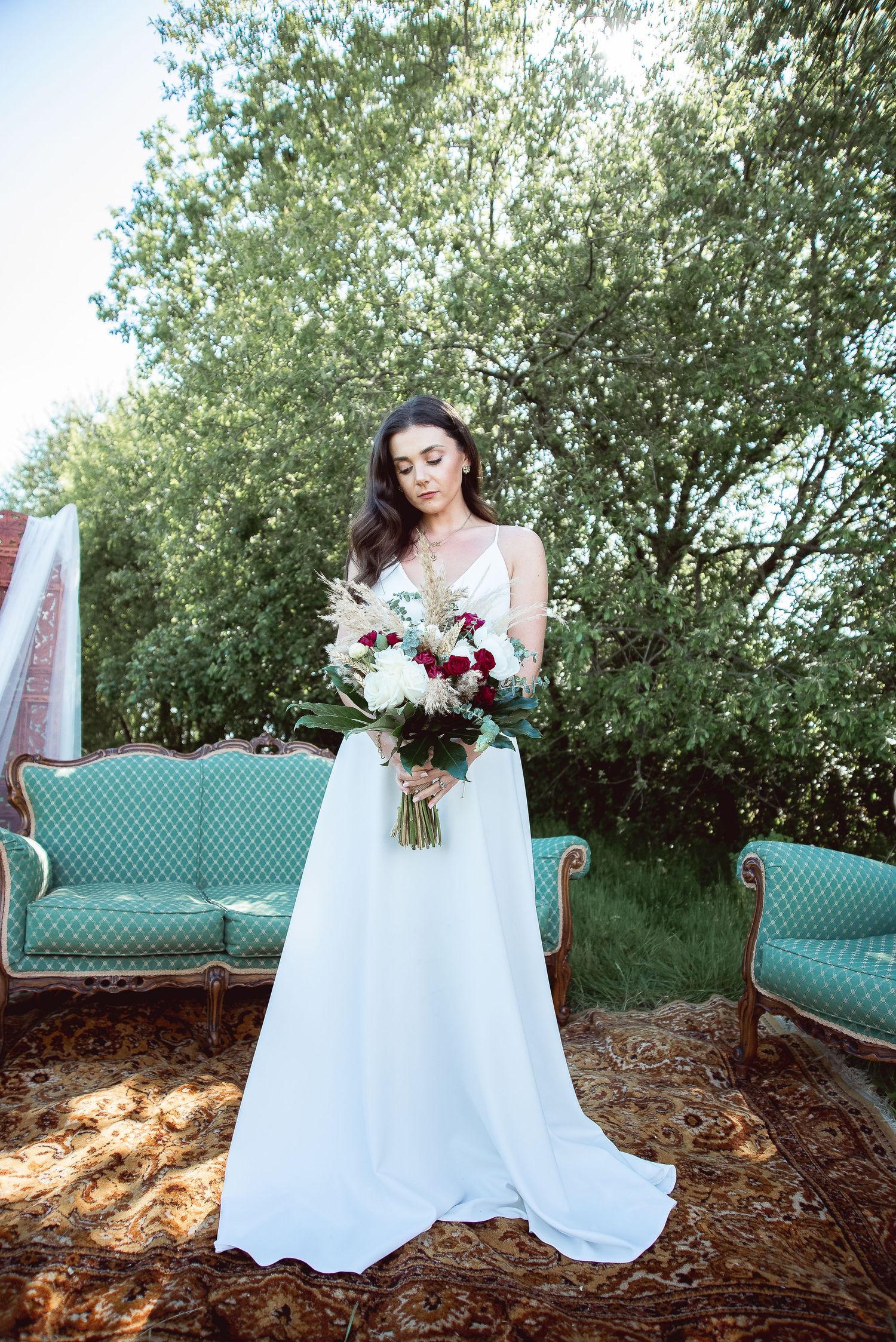 A white wedding dress flows elegantly across a mint green vintage sofa in an outdoor garden setting.