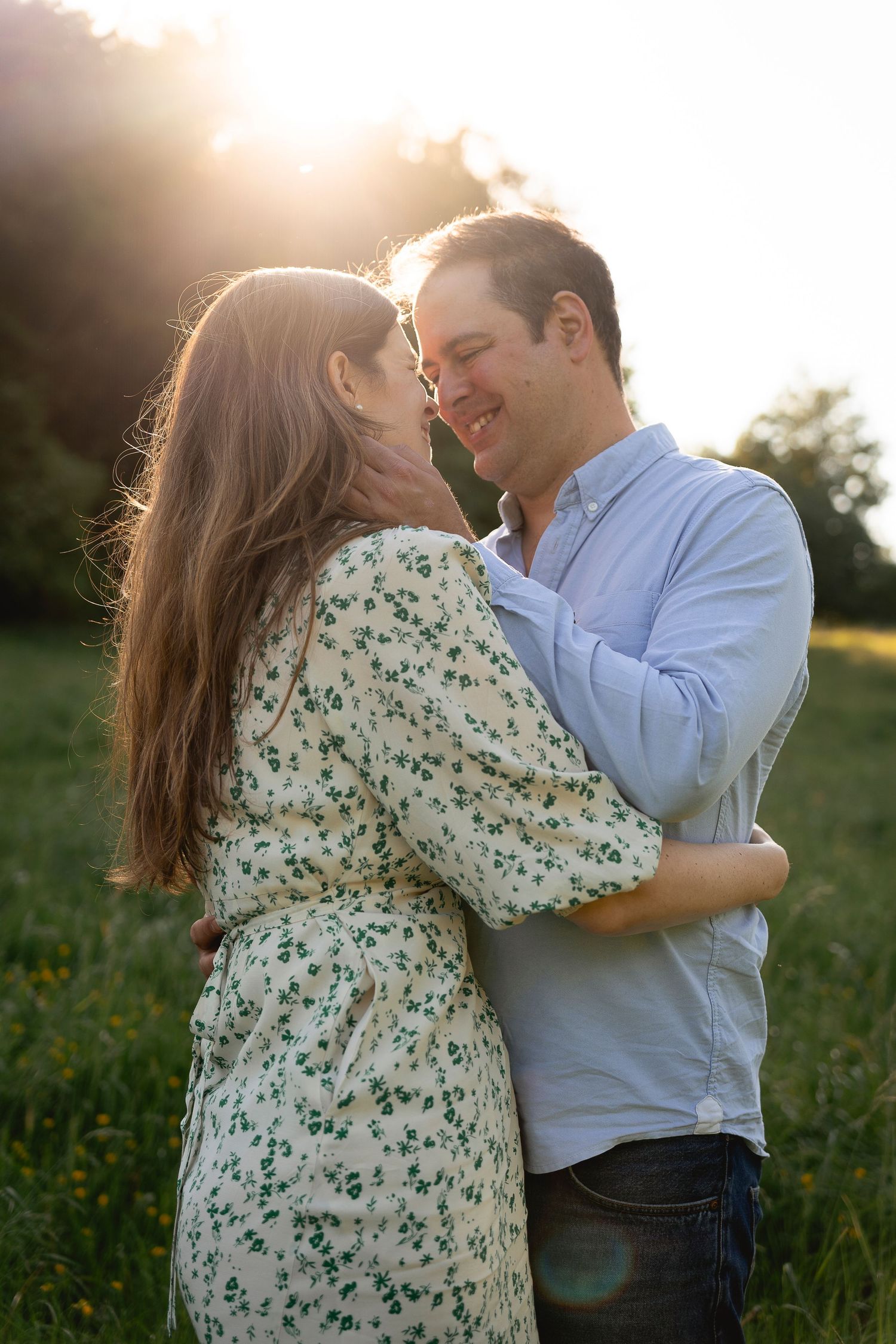 couple in the middle of field embracing and about to kiss, man stroking her cheek, sun shining behind them