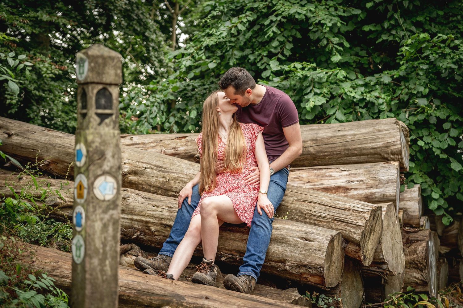 couple sitting back to front on a pile of logs kissing, woman sat between mans' legs,