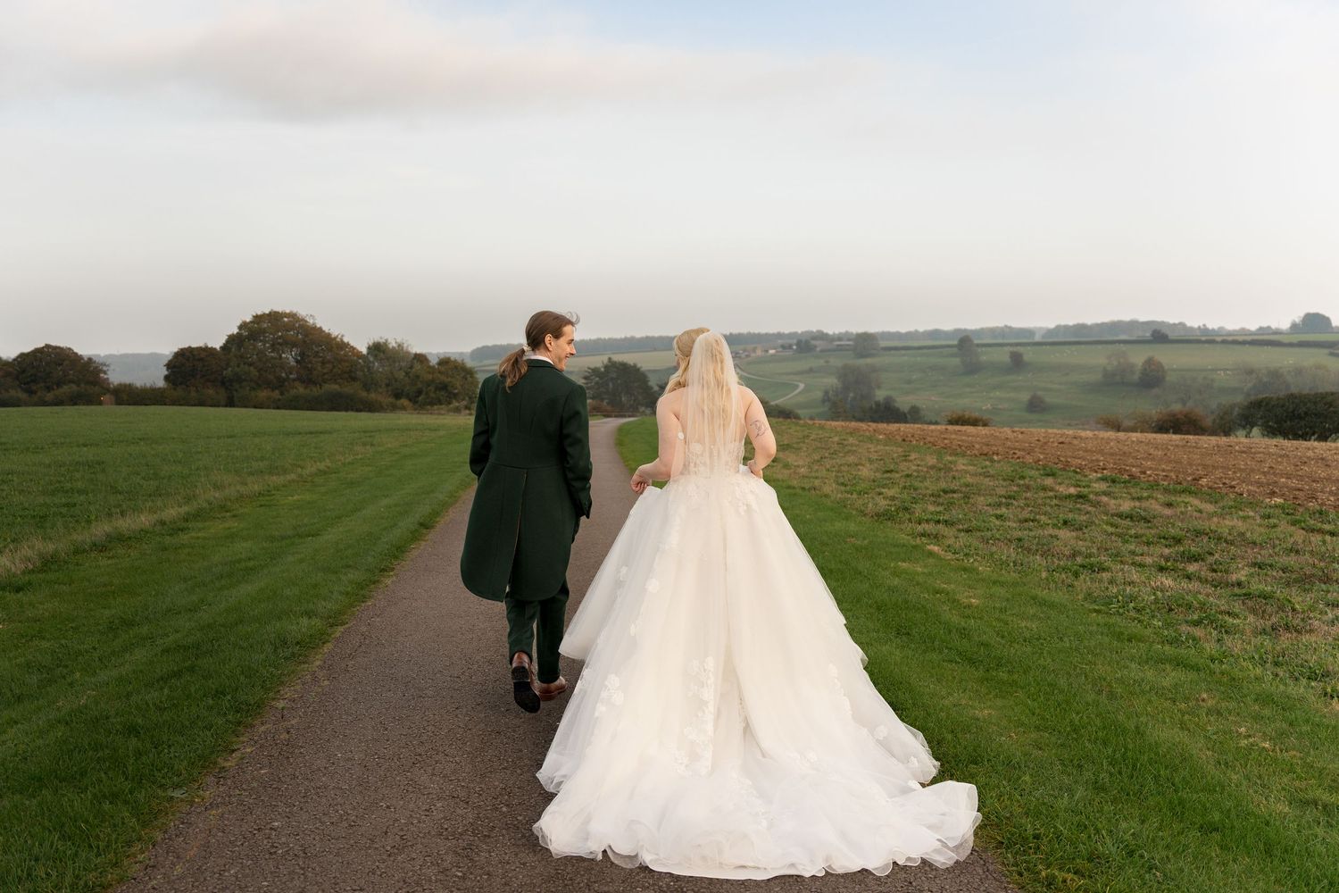 Bride and groom walking hand in hand along a scenic garden path on their wedding day.