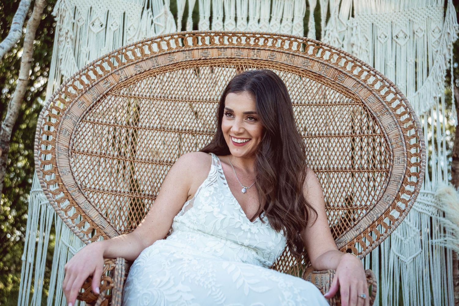 Elegant white lace wedding dress displayed against a macrame backdrop with a bohemian peacock chair.