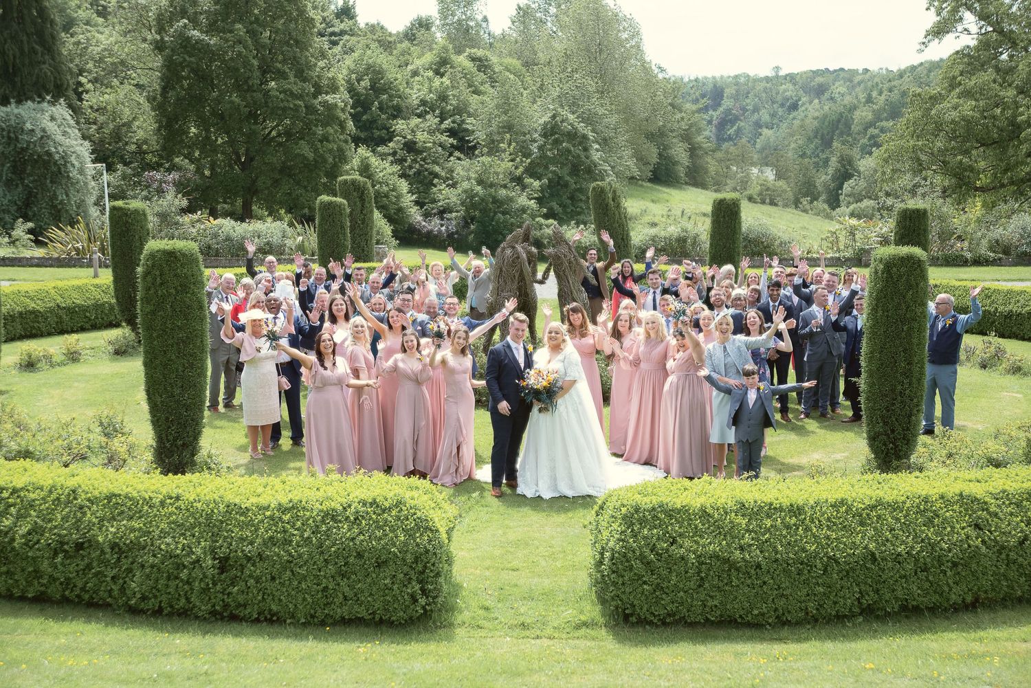 Aerial view of wedding party and guests gathered in formal garden surrounded by hedges.