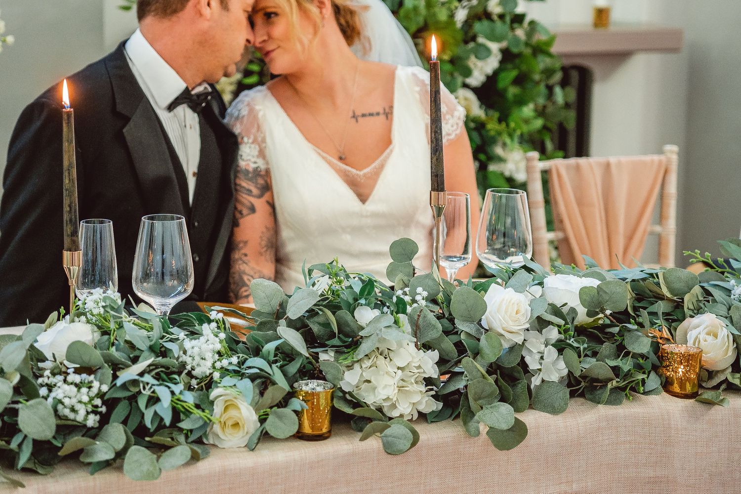 Close up of Greenery garland on top table with Bride and Groom kissing in the background