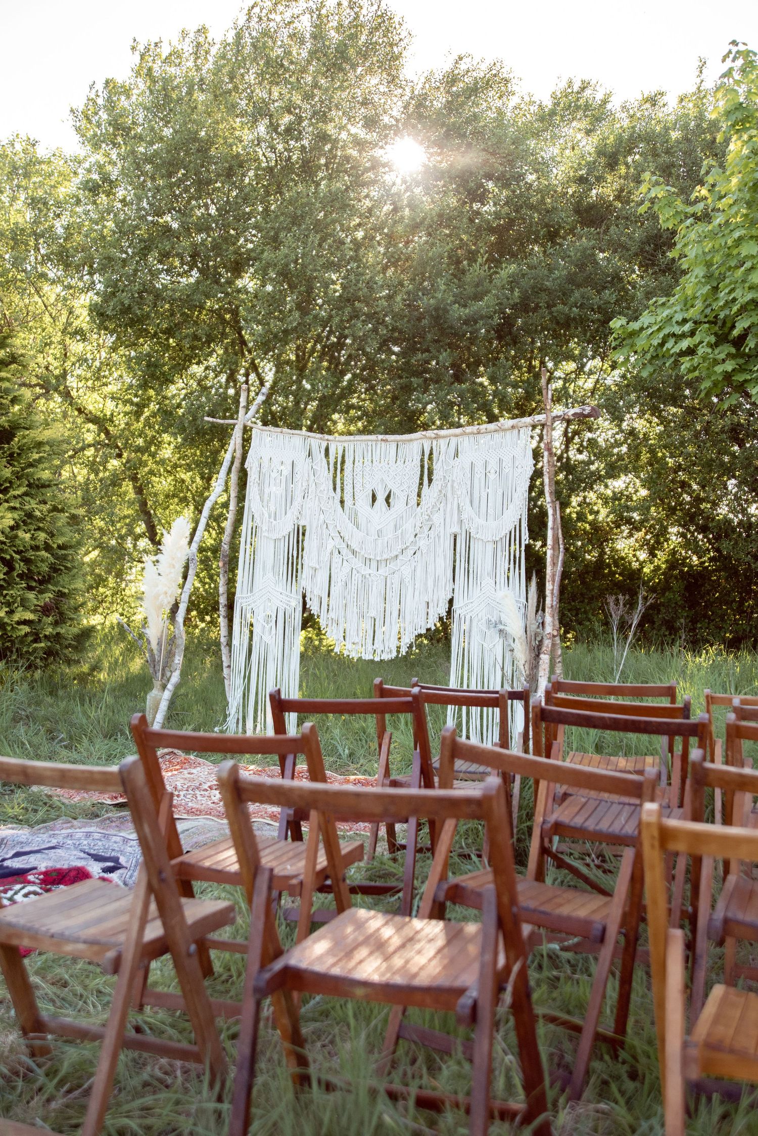 Wooden chairs arranged in rows facing a white macrame backdrop for an outdoor ceremony.
