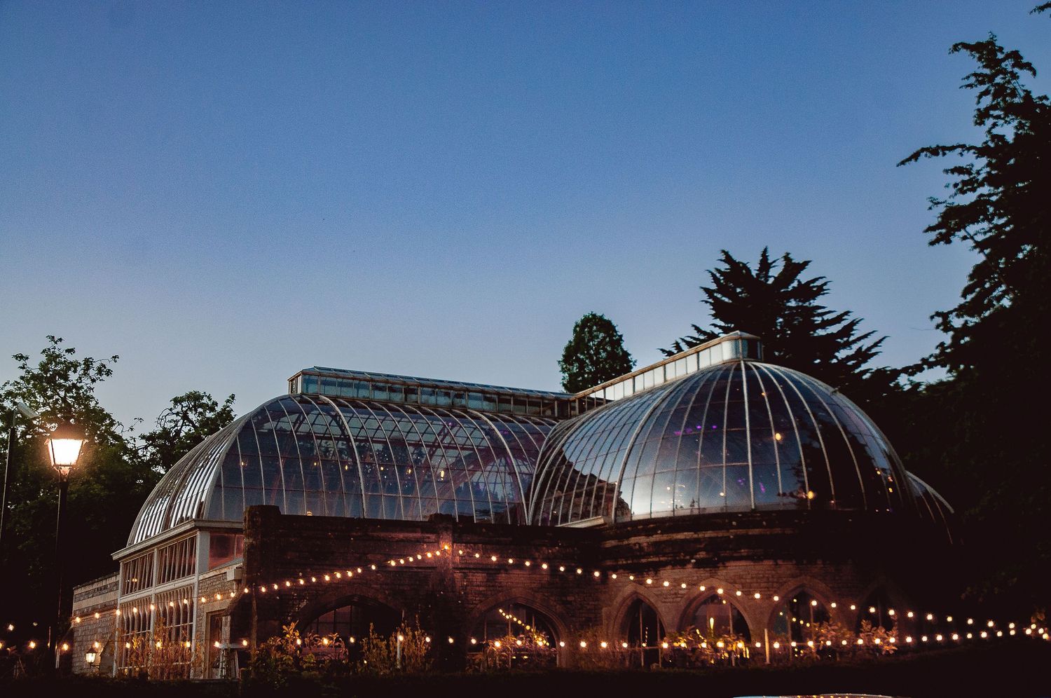 Evening view of illuminated glass conservatory with string lights.