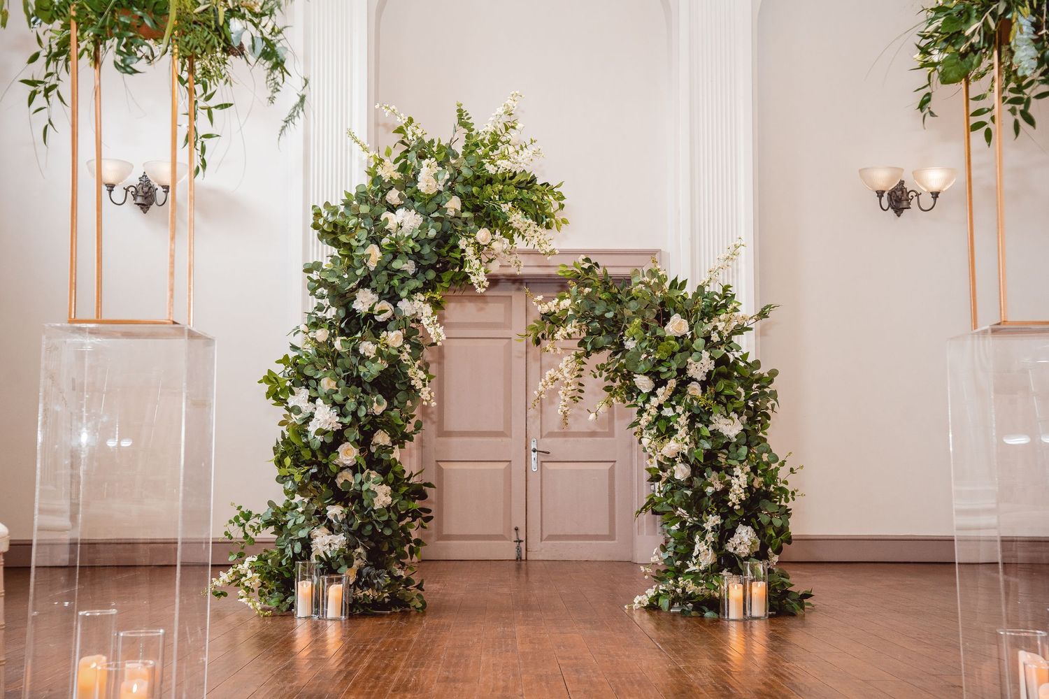 Broken arch ceremony decor with foliage and white flowers and pillar candles at the base