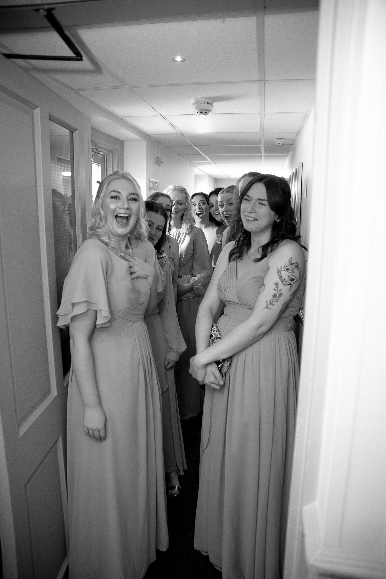 Wedding party members sharing laughter in a hallway wearing matching bridesmaid dresses.