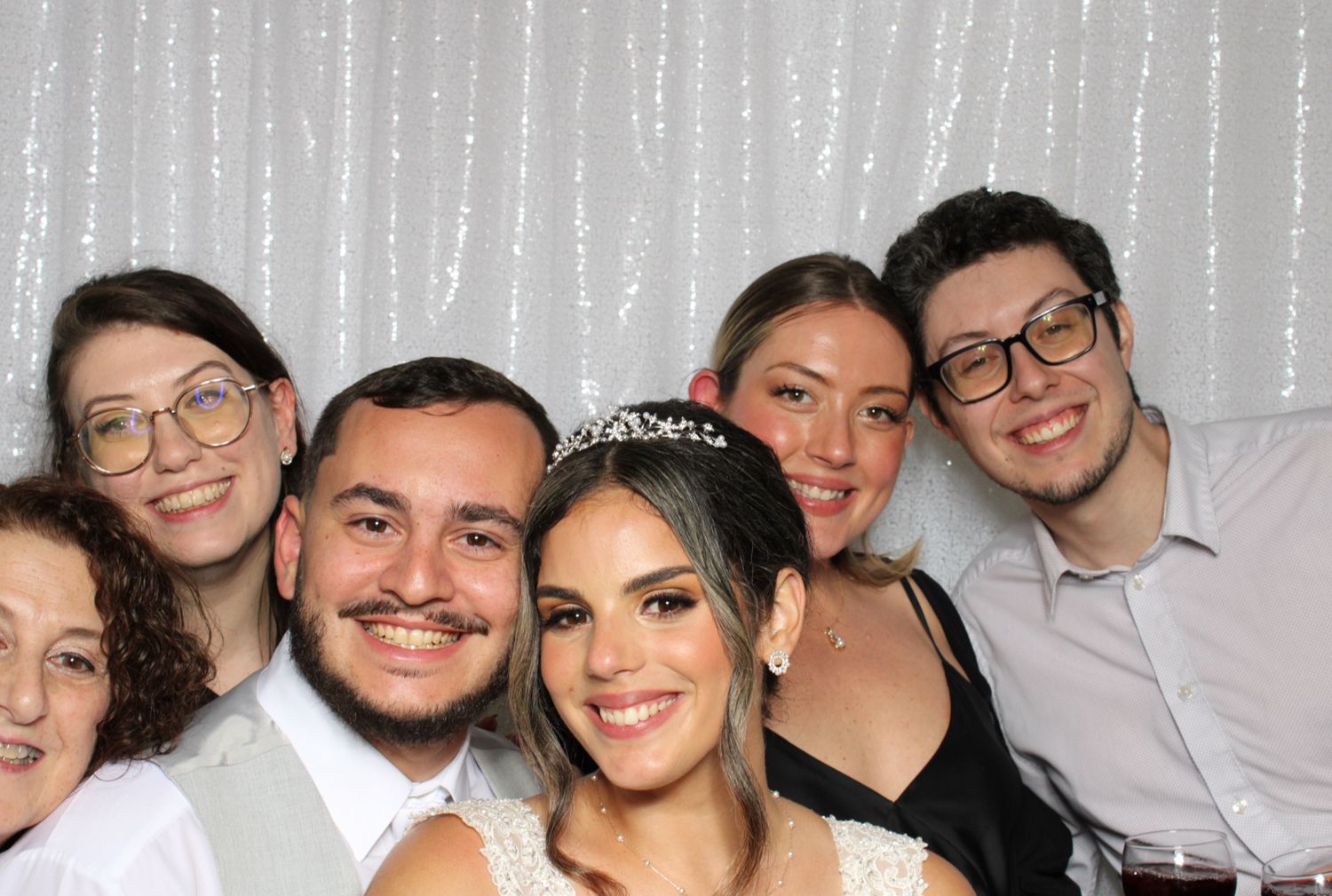 Wedding party group poses together in front of silver curtain backdrop.