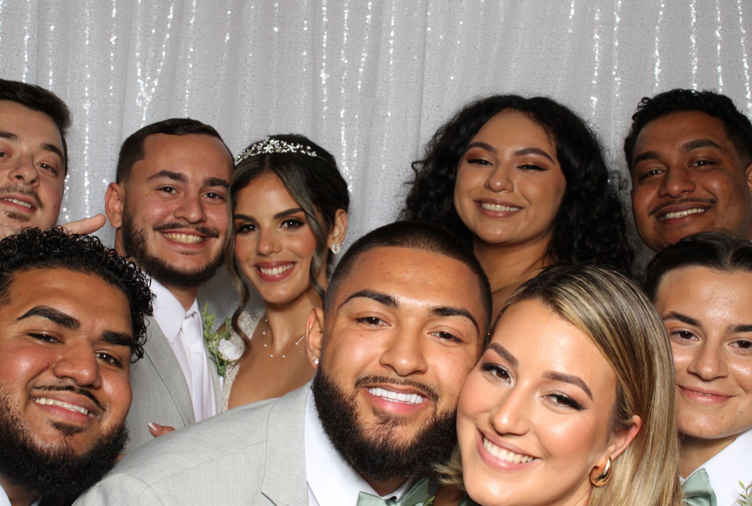 Group of friends and newlyweds posing together at a wedding reception photo booth, smiling happily.