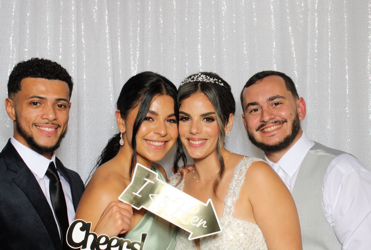 Wedding party poses with the bride holding cash in front of a silver curtain backdrop.
