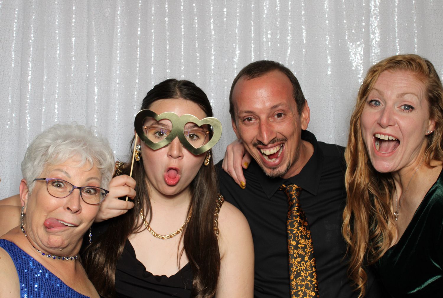 Group making silly faces and poses together in a photo booth with silver curtain background.
