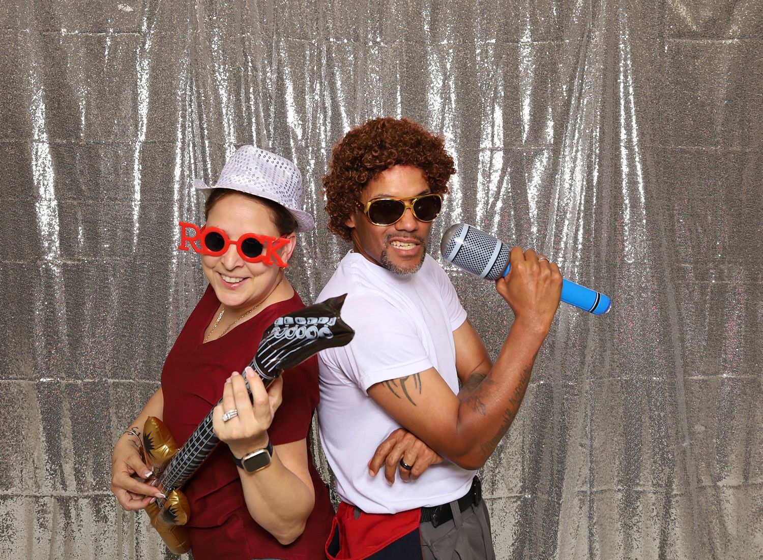 Two people in fun costumes pose with toy instruments and accessories in front of a silver sequin backdrop.