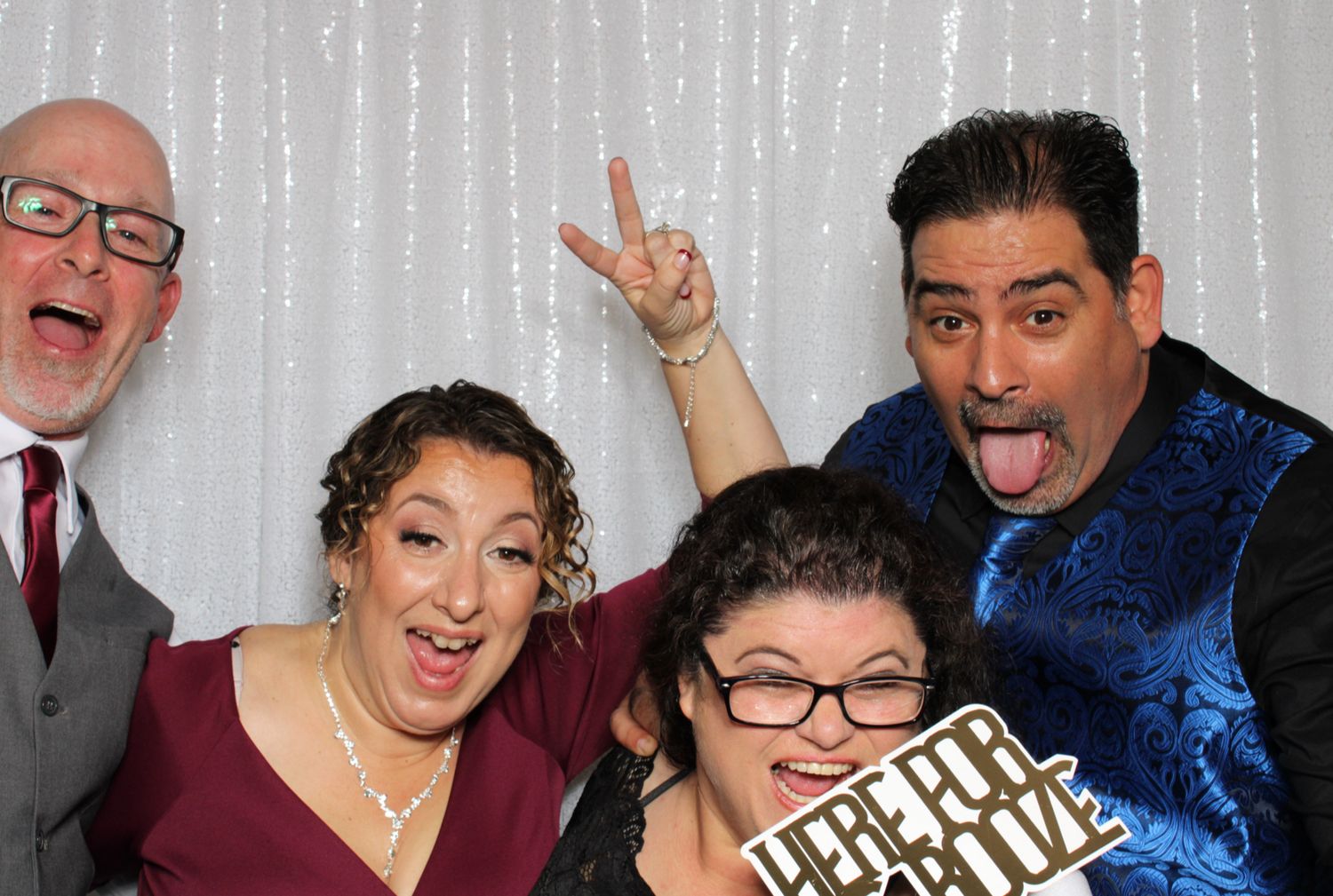 A group poses energetically against a silver backdrop in a photo booth with one person making a peace sign.