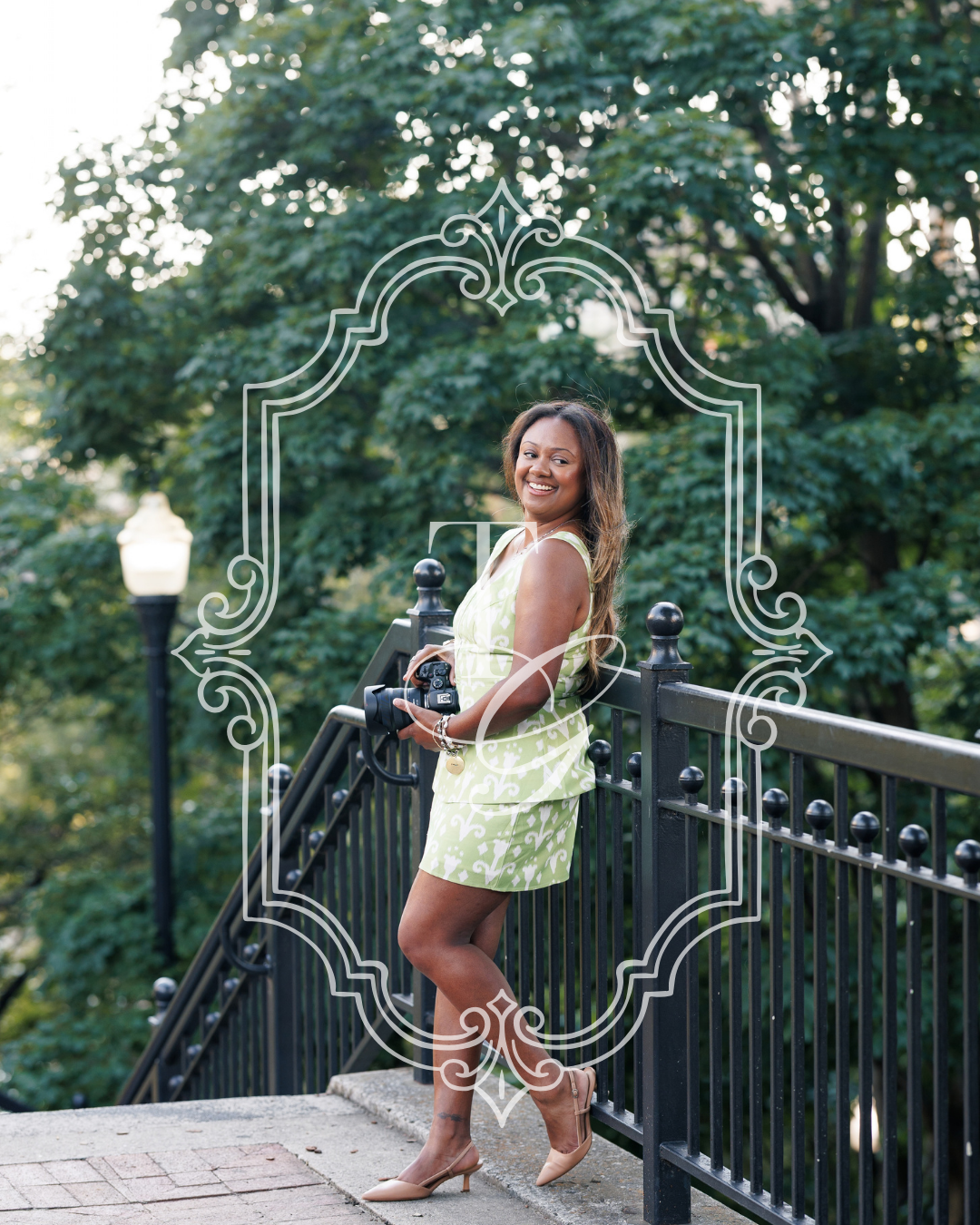 Woman in green dress holding camera on bridge, surrounded by lush trees and decorative frame overlay.