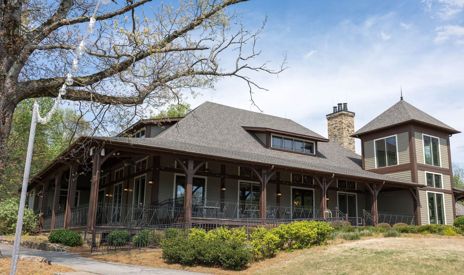 Large craftsman-style home with wrap-around porch, stone chimney, and turret surrounded by mature trees and landscaping.