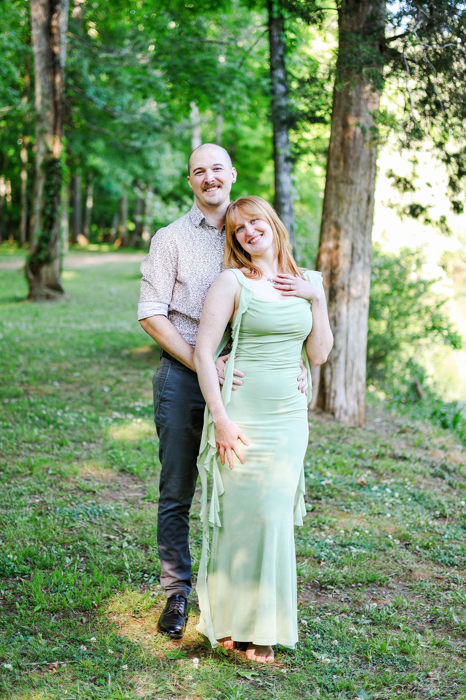 Happy couple embracing outdoors in a green park, woman in mint dress, bald man in casual shirt, smiling together.