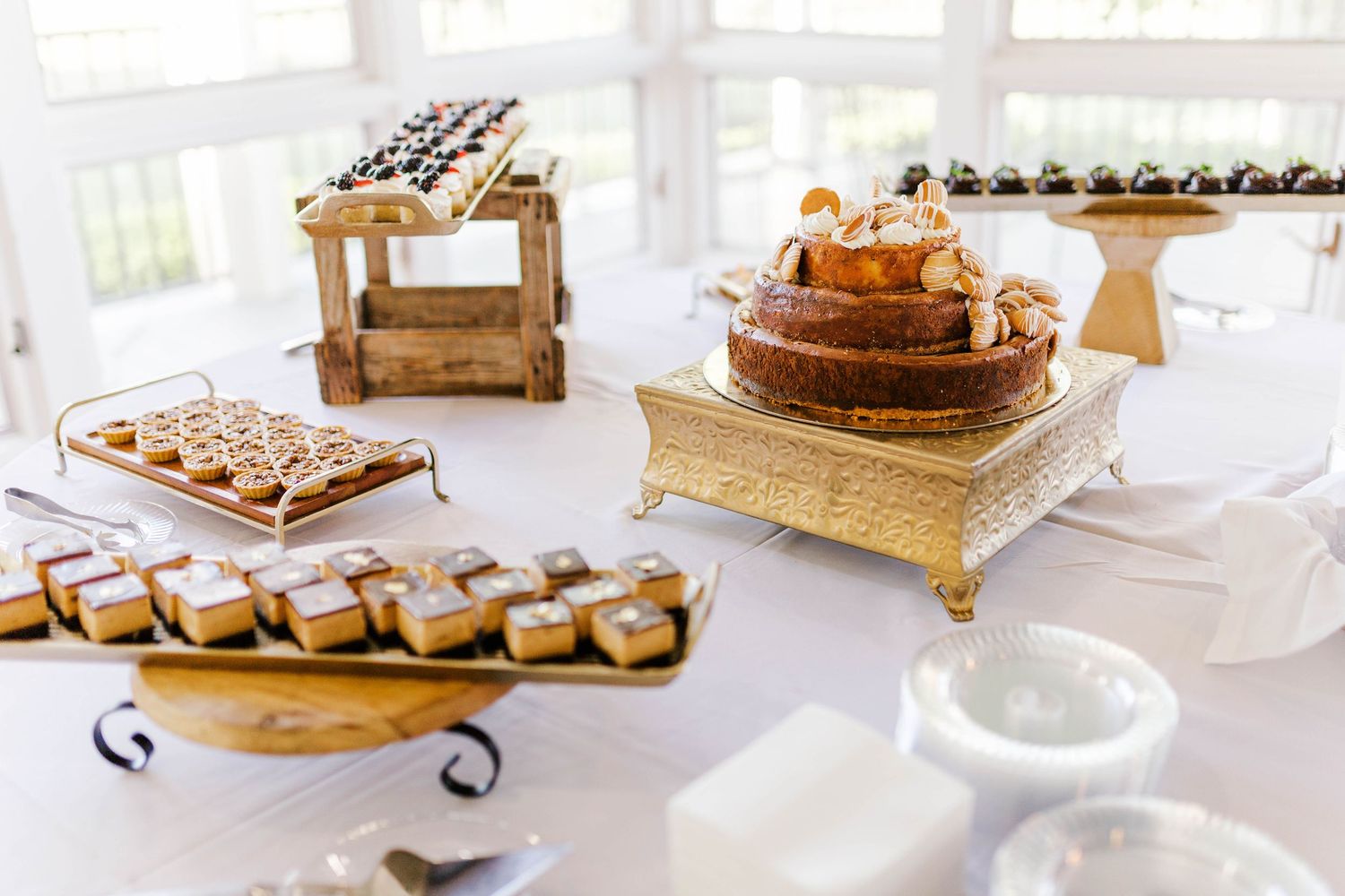 Elegant dessert table with gold cake stand, layered cake, petit fours, and assorted sweets at a wedding reception.