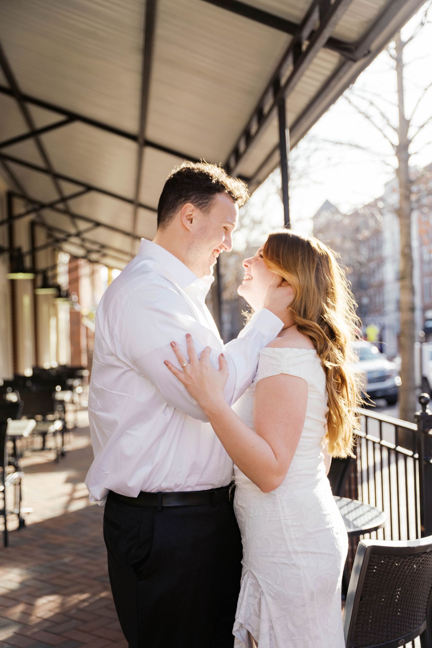A couple in wedding attire embraces and smiles at each other on a sunlit outdoor patio.