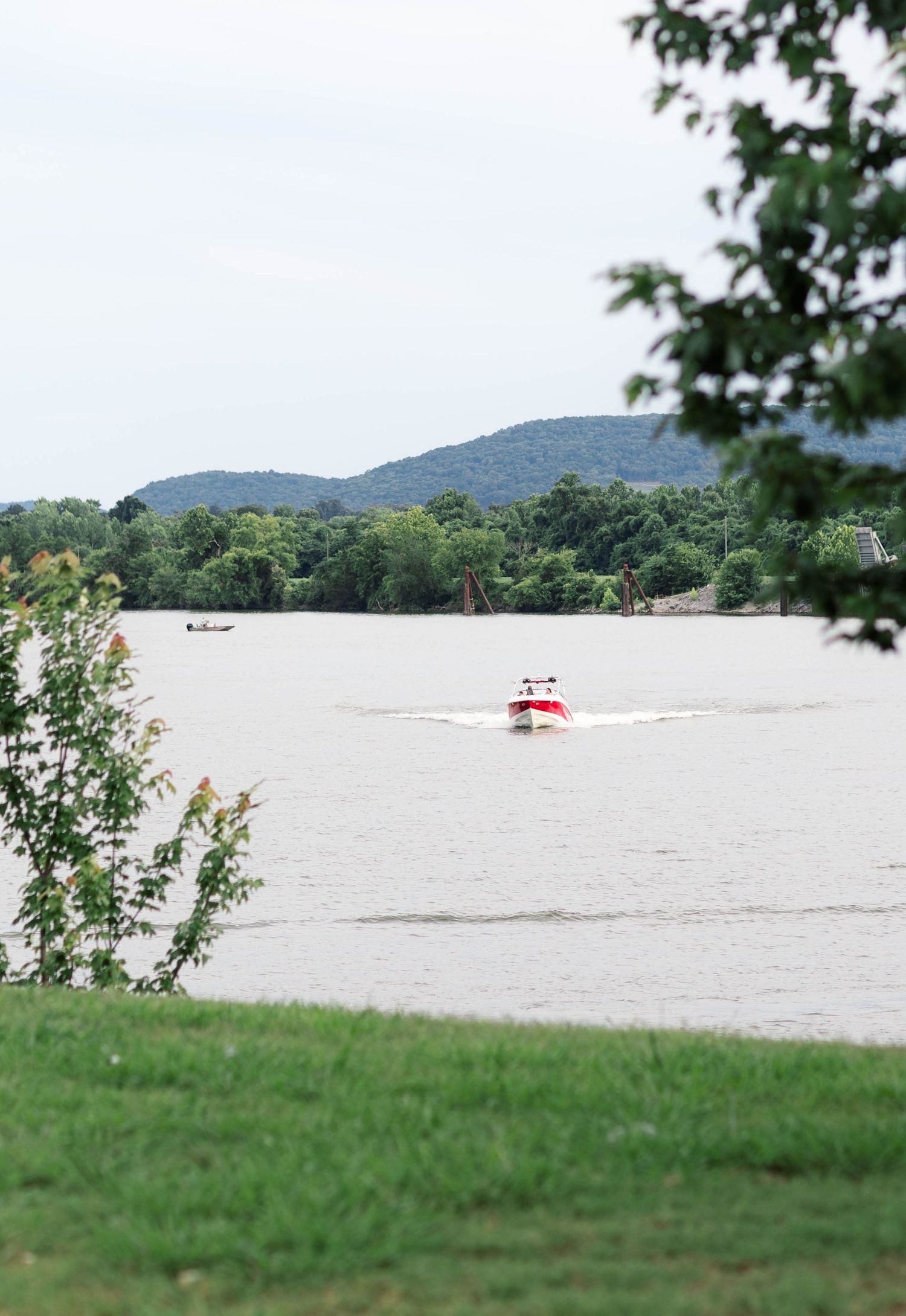 A red speedboat creates a wake on a calm river with lush green hills in the background.