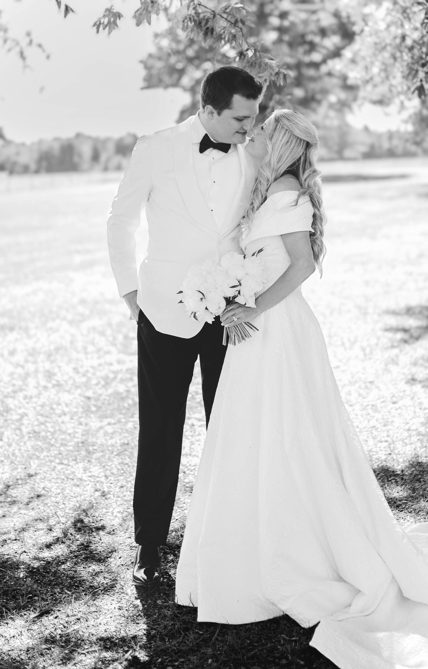 Black and white photo of a bride and groom sharing a romantic kiss outdoors on their wedding day.
