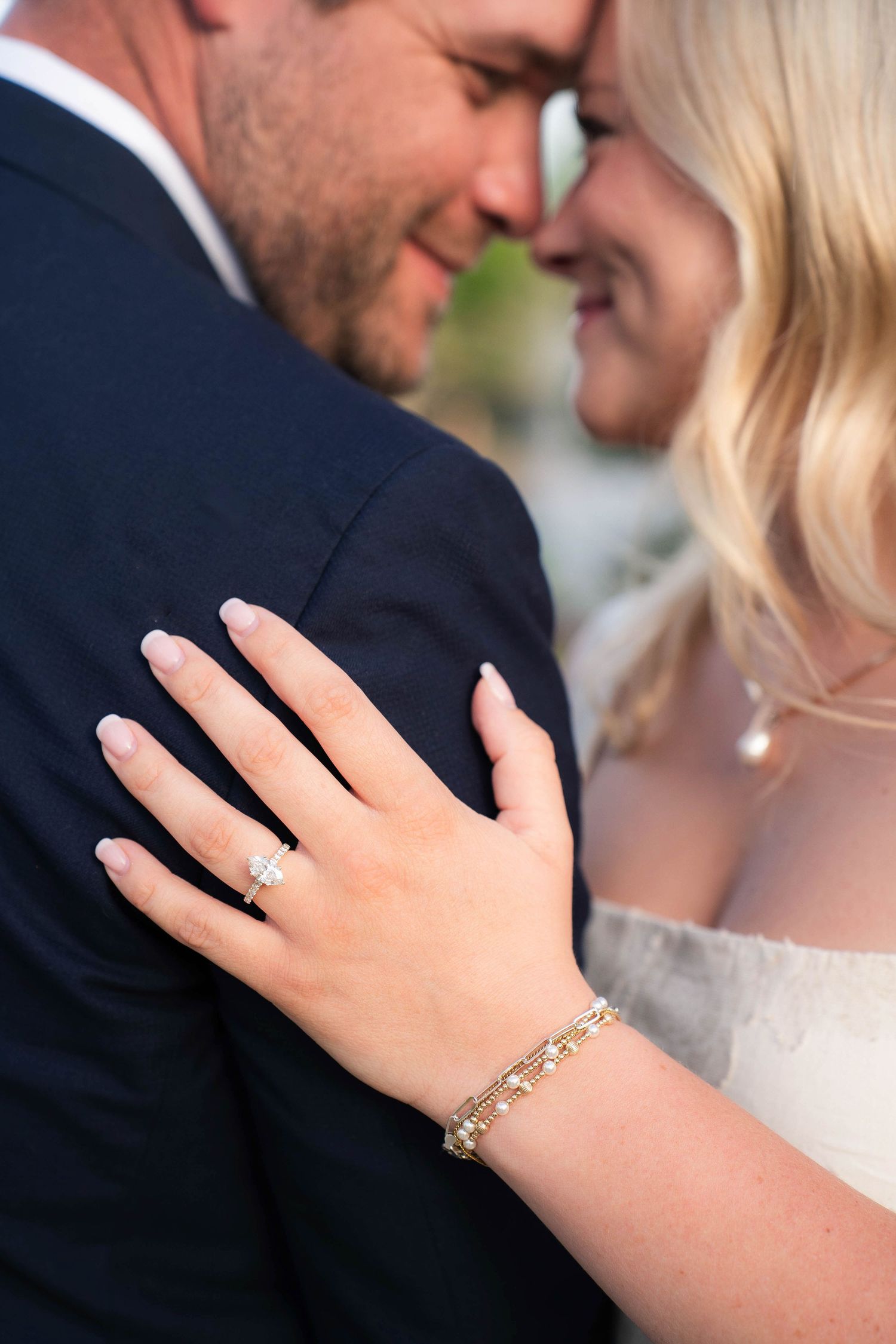 Bride and groom touching foreheads, showcasing diamond engagement ring and gold bracelet on bride's hand.